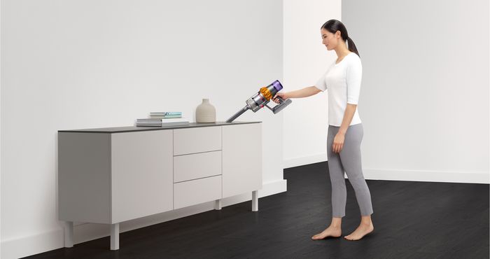 Žena vysává horní desku komody vysavačem přestavěným na ruční