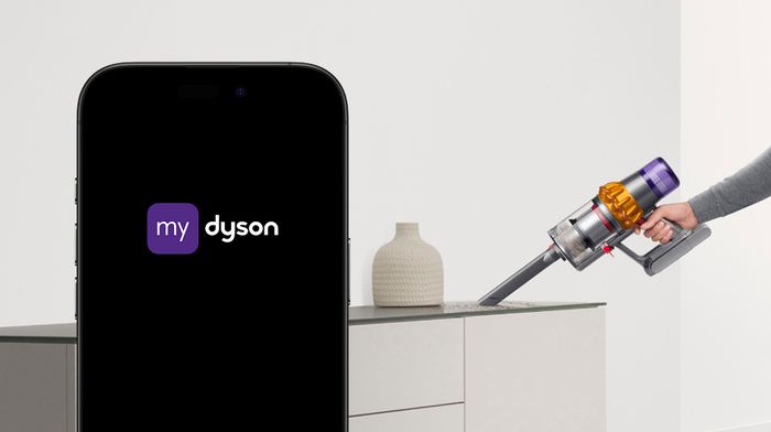 Telefon s aplikací MyDyson, vedle něj vysavač při úklidu komody