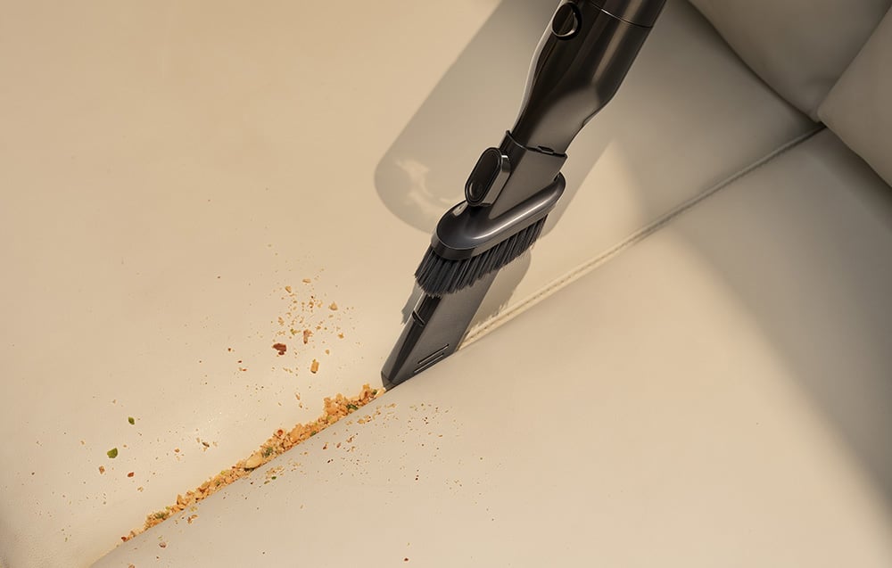 A vacuum cleaner with a multifunctional nozzle removes crumbs from a gap in a couch.