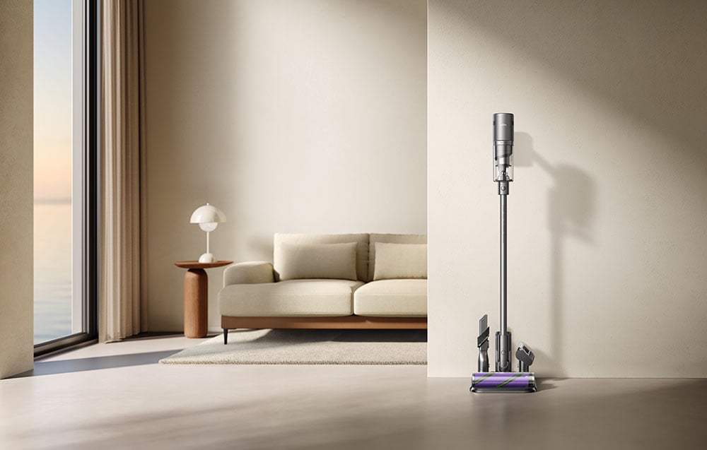 Upright vacuum cleaner in station with accessories stands against the wall.
