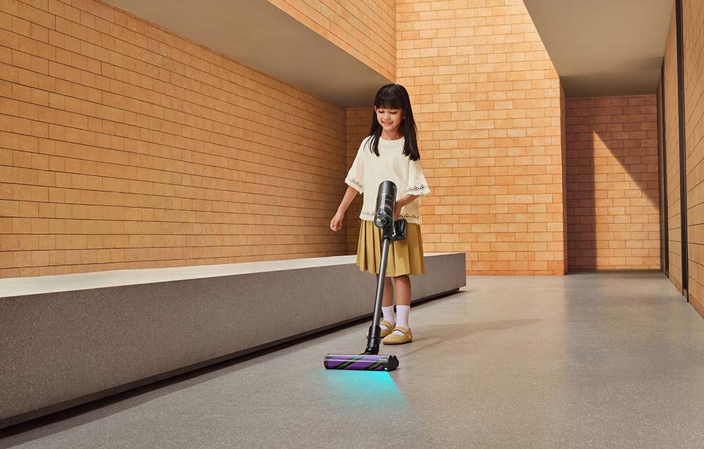 The girl vacuums the floor with an upright vacuum cleaner with a light.