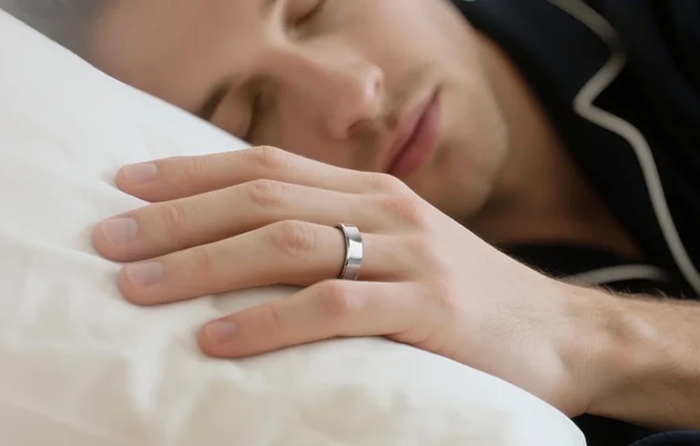 Muž v pyžamu spí s rukou na polštáři, na prstu má stříbrný chytrý prsten