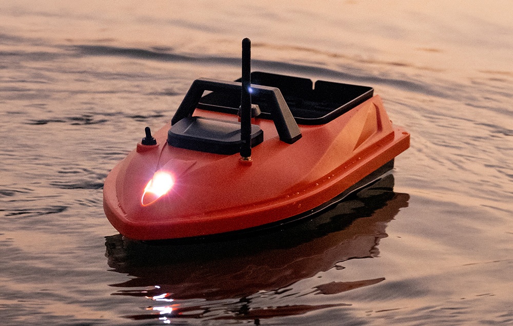 Oranžová krmná loď s jasným reflektorem svítícím na přídi za soumraku.