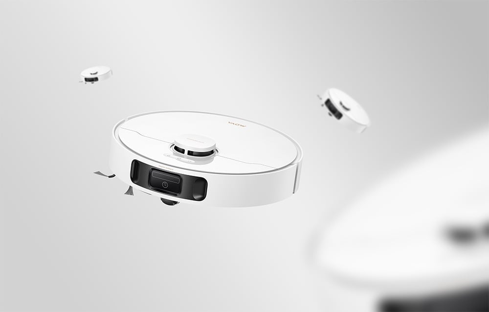Čtyři bílé čisticí roboty Mova v pohybu na šedém pozadí, s jedním v popředí